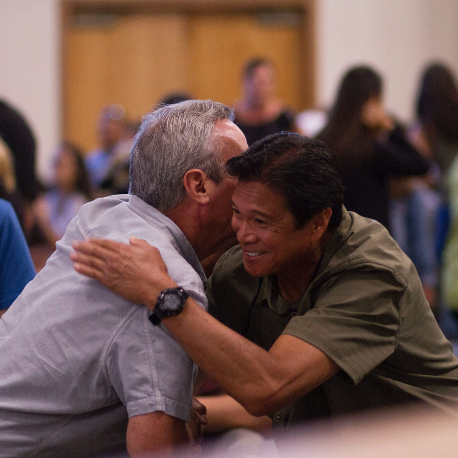 Two men hugging amongst crowd in an auditorium