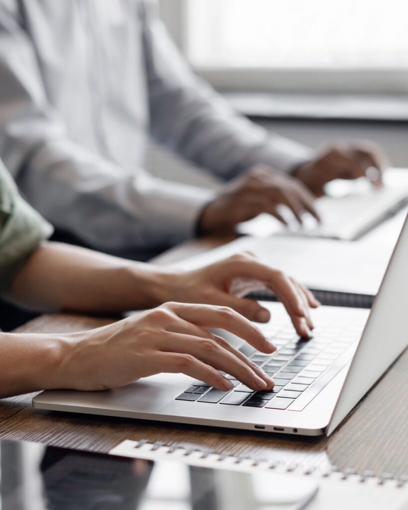 Picture of two people's hands typing on computers side by side.