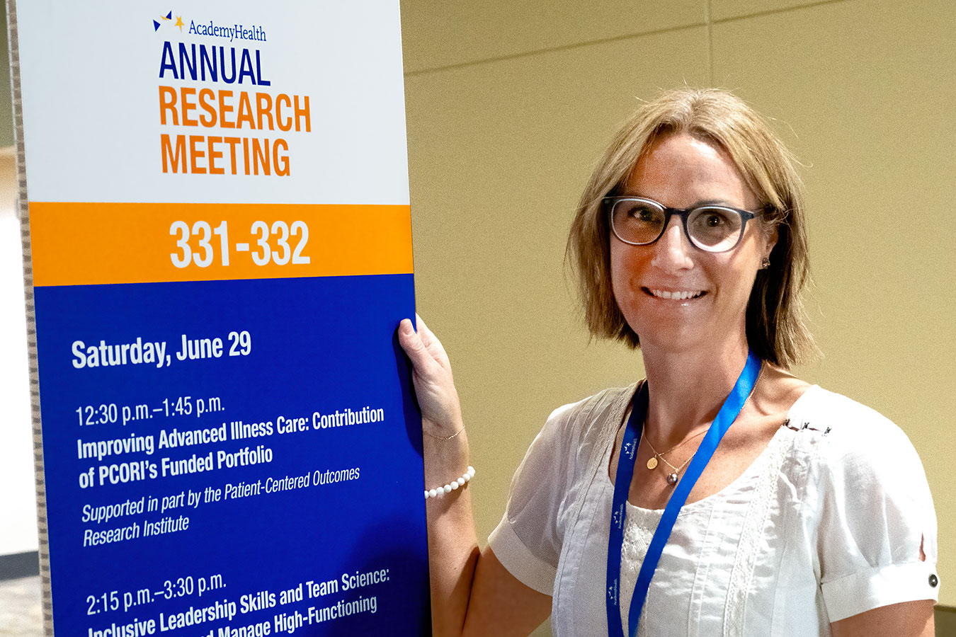 Kate Courtright poses with a sign at the Annual Research Meeting, with the title of her session, "Improving Advanced Illness Care: Contribution of PCORI’s Funded Portfolio."