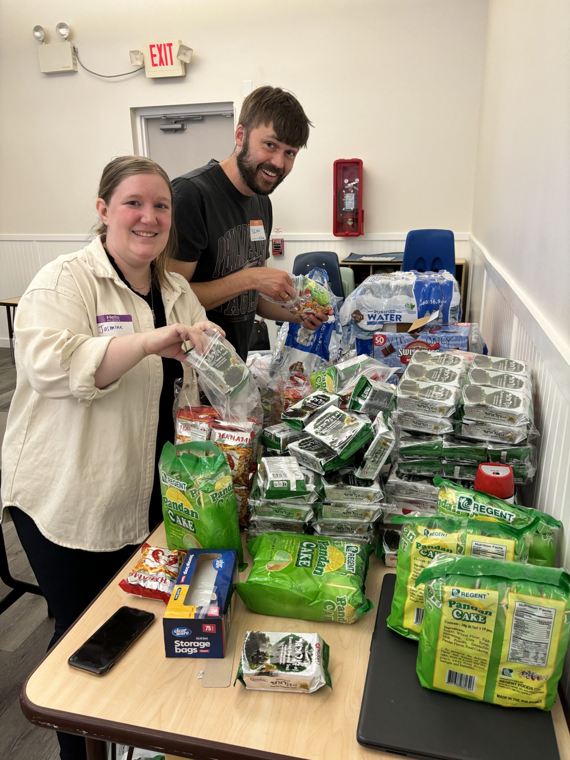 Jasmine Silvestri and Brian Bayes smile at the camera while packing snacks into plastic bags.