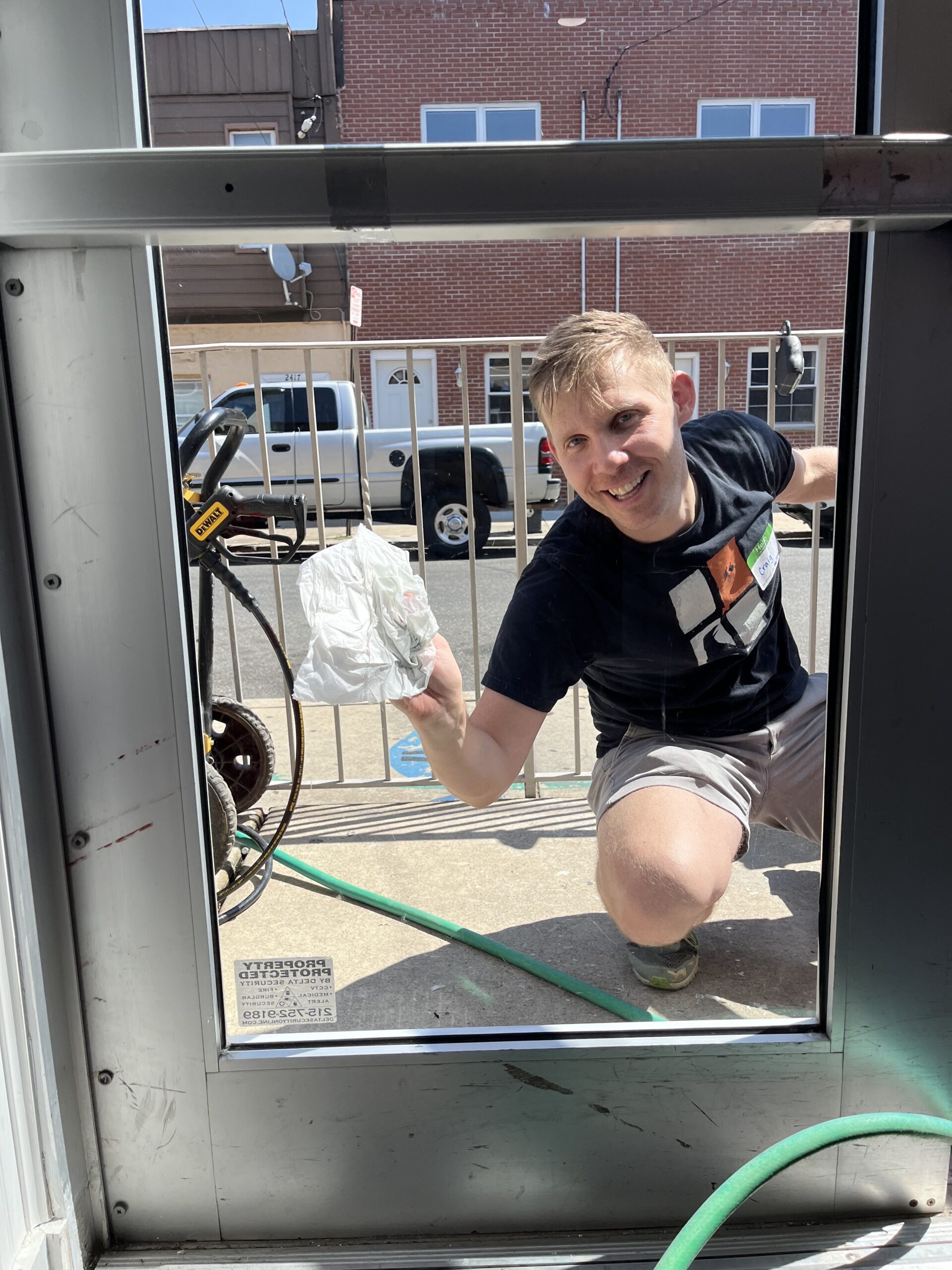 Craig Kwiatkowski smiles through the glass door as he cleans it from the outside with a paper towel. 