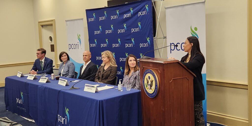 Eric Moody, Joanna Hart, Scott Halpern, Christie Befort, and Sarah Ruiz sit on as a panel in front of a PCORI backdrop. Another researcher stands at the podium.